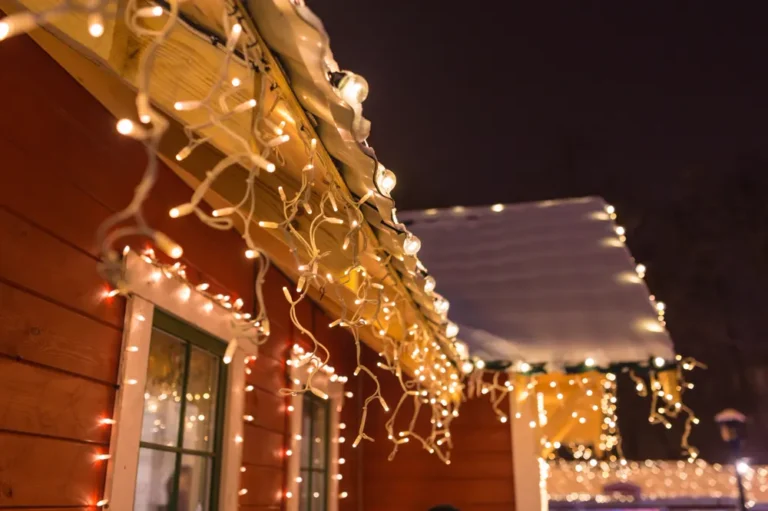 Warm white icicle and globe lights hung along a snowy eave and window trim