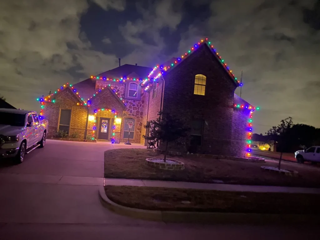 Multicolor C9 Christmas light installation following the peaks and gables of a two-story brick home in North Texas
